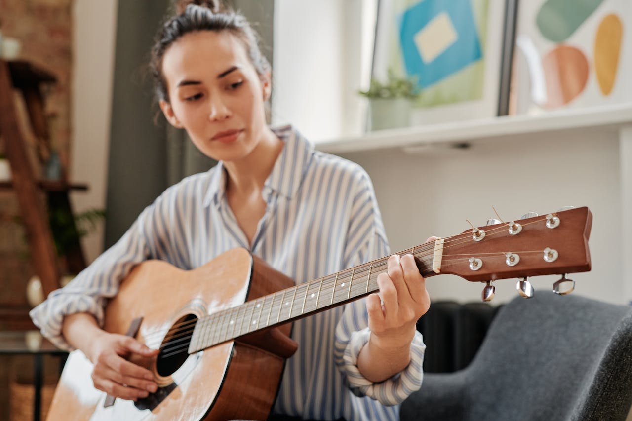 Young woman playing acoustic guitar in a cozy indoor setting.