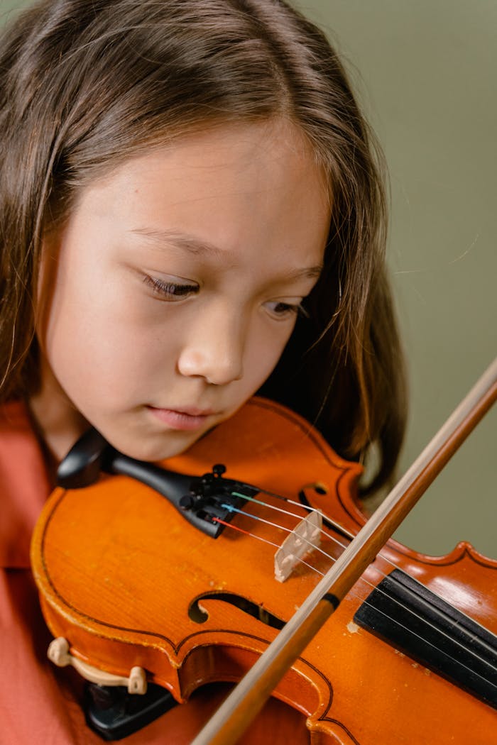 A focused young girl playing the violin with concentration in a close-up shot.